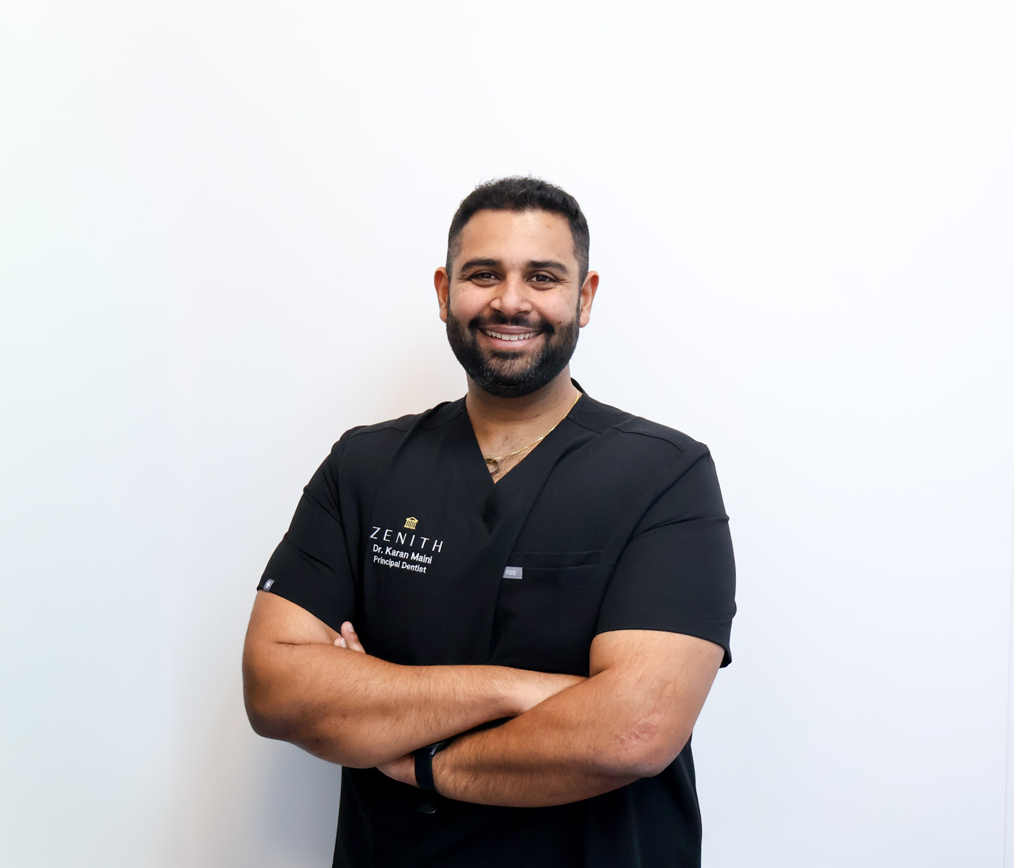 Dr Karan Maini smiling with arms crossed, wearing branded scrubs